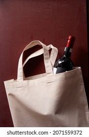 A Vertical Shot Of A Bottle Of Wine In An Eco-friendly Tote Bag On A Red Background