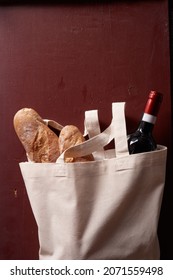 A Vertical Shot Of A Bottle Of Wine And Fresh Baguettes In A Tote Bag On A Red Background