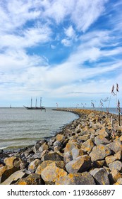 Vertical Shot Of Breakwater Or Pier And Poles With Colored Rope And Plastic Waving In The Wind And A Ship In The Wadden Sea At The Entrance To The Port Of Harlingen The Netherlands             