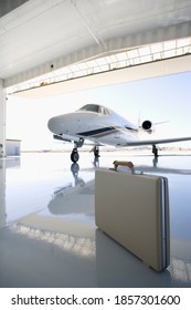 Vertical Shot Of A Briefcase On The Floor Of A Hanger By Executive Jet In The Background.