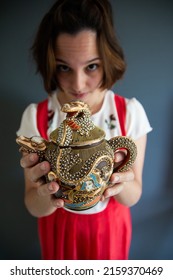 A vertical shot of a caucasian female holding a beautiful teapot with Asian ornaments