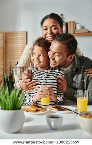 vertical shot of cheerful african american family hugging warmly each other at breakfast table