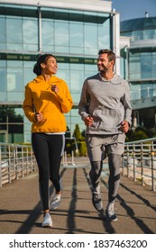 Vertical Shot Of A Cheerful Mixed Race Couple Jogging Outdoors In Sportswear Together