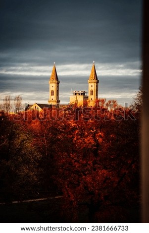 A vertical shot of church towers behind autumn-colored trees