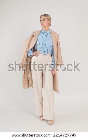 Vertical shot of confident blond businesswoman in formal stylish outfit with jacket on shoulders posing on white studio background. Fashionable worker in office suit, lady boss in office. Copy space
