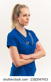 Vertical Shot Of A Confident Strong Female Doctor. Beautiful Caucasian Woman With Tied Up Blond Hair In Dark Blue Clinic Uniform And Stethoscope. Crossed Arms, Positive Facial Expression. White