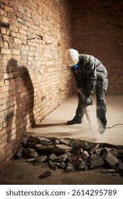 Vertical shot of construction worker using new jackhammer to destroy cement on floor, he wearing uniform and respirator to protect himself from dust