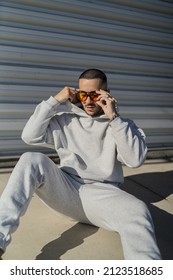 A vertical shot of a cool stylish young male with orange sunglasses and a gray sweatsuit posing
