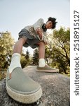 Vertical shot of cool teenage Black boy in playful mood posing for camera with foot in front while walking in city park, fisheye effect