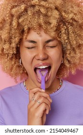 Vertikale Aufnahme von geschmeidig haarigen Feamle Modell verwendet Zungenschrott kümmert sich um Mundhygiene gekleidet in violettem T-Shirt sauber den Mund in geschlossenen Räumen. Junge schöne Frau benutzt regelmäßig Zungenreinigung