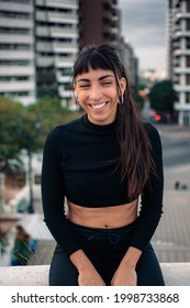 A vertical shot of a cute Argentinian girl smiling delightfully in the city with a blurred background