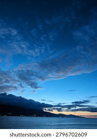 A vertical shot of dramatic blue hour sky with dark clouds over a mountain silhouette