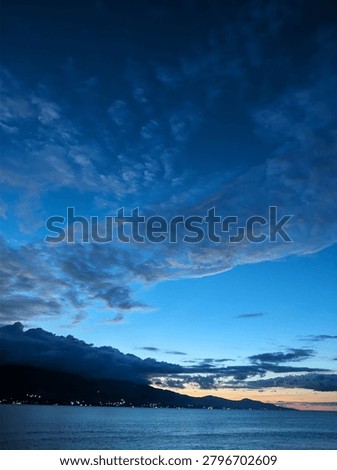 A vertical shot of dramatic blue hour sky with dark clouds over a mountain silhouette