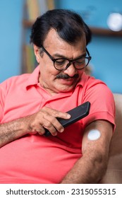 vertical shot of Elderly senior man checking glucose level by tapping smartphone to monitoring sensor at home - concept of health care, technology and mdicare. - Shutterstock ID 2315055315