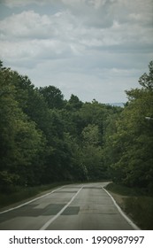 A vertical shot of an empty road surrounded by trees on a cloudy day