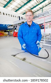 Vertical Shot Of An Engineer In Uniform Inspecting Airplane Parts At A Hangar And Smiling At The Camera.