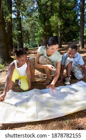 Vertical Shot Of A Family Playing Treasure Hunt And Looking Into A Map For Treasure In The Forest.