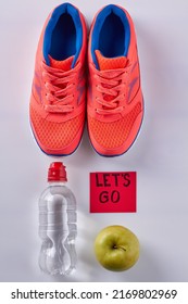 Vertical shot flat lay pair of shoes with water bottle and green apple. Sticker note with lets go inscription.