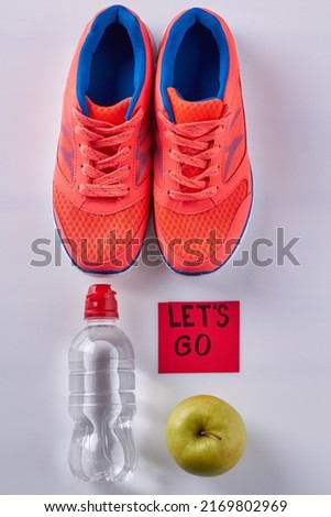 Vertical shot flat lay pair of shoes with water bottle and green apple. Sticker note with lets go inscription.