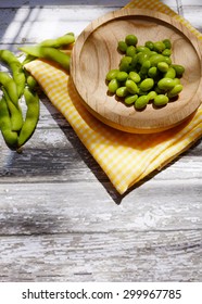 Vertical shot of green soybeans on a wooden plate below the sunlight rays