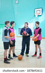 Vertical Shot Of A Gym Teacher Teaching Basketball To A Group Of High School Students In A Gym.