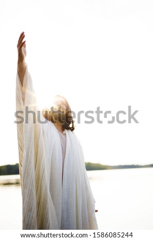 A vertical shot of the Jesus Christ with his hand up towards the sky while the sun shines near his head