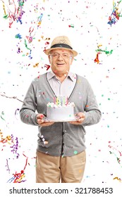 Vertical Shot Of A Joyful Senior Gentleman Carrying A Birthday Cake With Party Streamers Flying All Around Him Isolated On White Background