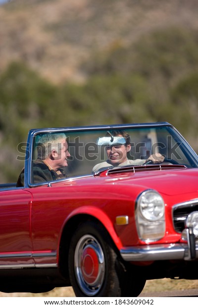 Vertical shot of a joyous\
father and son driving in a red convertible on a sunny day with\
copy space.