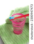 A vertical shot of a kiddie red toothbrush on a plastic cup and bath towel