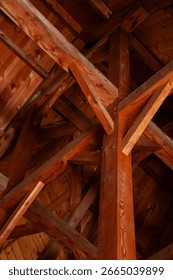 A vertical shot looking up at the complex and intricate pattern of exposed wooden beams and rafters in the ceiling of a rustic cabin or cottage.