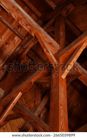 A vertical shot looking up at the complex and intricate pattern of exposed wooden beams and rafters in the ceiling of a rustic cabin or cottage.
