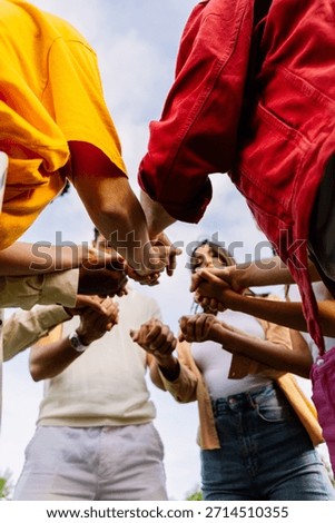Vertical shot. Low angle view of united group of young people in circle holding hands. Community, support and teamwork concept with millennial people showing unity outdoors.