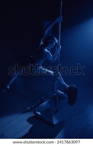 Vertical shot of man doing spin on pylon top while his female dancing partner working on floor in dim blue light