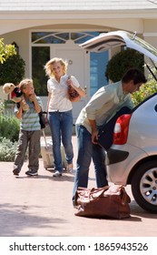 Vertical Shot Of A Man Loading Bags In The Boot Of A Car With A Woman And Kid Walking Towards The Car In The Background.