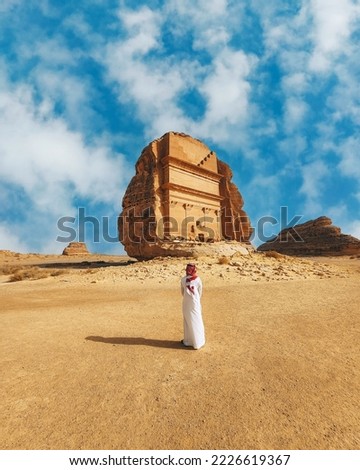 A vertical shot of a man standing in front of the Tomb of Lihyan son of Kuza in Saudi Arabia