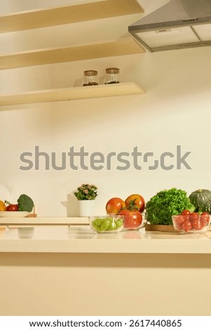 Vertical shot of marble dining table with fresh organic vegetables. Modern extractor hood installed above. Spice jars placed on wooden shelves. Cozy and bright kitchen with flower pots around.