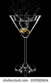 A vertical shot of martini glass with olive and splashes on black background