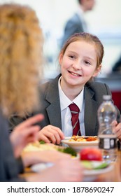 Vertical Shot Of A Middle School Student Eating Lunch And Talking To A Friend In The School Cafeteria.