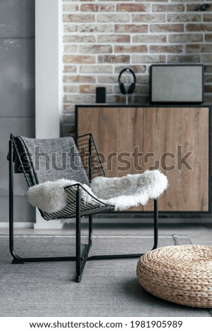 Vertical shot minimalist interior of contemporary apartment with stereo speaker nearby of wireless headphones and smartphone on brown shelf against brick wall. Metal chair with straw ottoman on floor