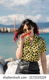 Vertical Shot Of A Modern Caucasian Woman Eating A Red Liquorice Candy Against The Backdrop Of A Sea.