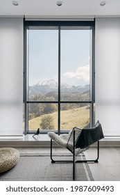 Vertical Shot Of Modern Metal Chair On Gray Carpeted Floor In Front Of Large Window With Amazing Mountain Landscape In Light Coloured Living Room. Minimalist Interior Design In Hotel Room Or House