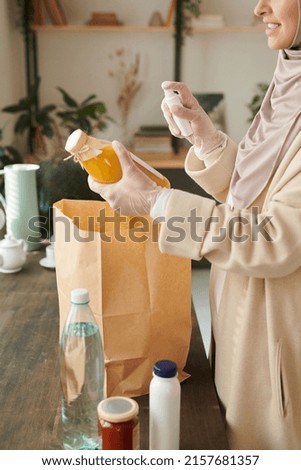 Vertical shot of modern young Muslim woman wearing protective gloves disinfecting things delivered to her during quarantine time