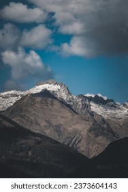 A vertical shot of a mountain range partially covered with snow under the cloudy sky