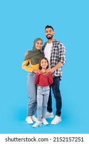 Vertical Shot Of Muslim Family Embracing Smiling To Camera Together Standing In Studio Over Blue Background. Islamic Father And Mother In Hijab Hugging Their Kid Daughter - Shutterstock ID 2152157251