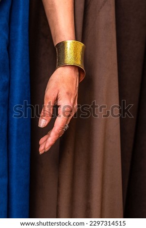 A vertical shot of an older woman's hand wearing a gold cuff bracelet