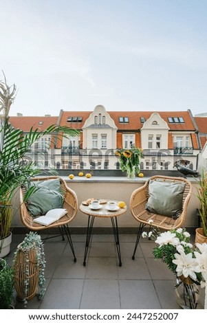 Vertical shot of open space on summer terrace, balcony on roof of hotel with view of cityscape. Wicker armchairs with cushions, round coffee table with breakfast against old historical city center