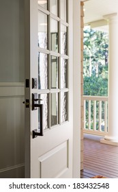 Vertical Shot Of An Open, Wooden Front Door From The Interior Of An Upscale Home With Windows. 