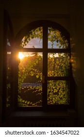 A Vertical Shot Of An Opened Arched Window With The Sun Shining In The Background