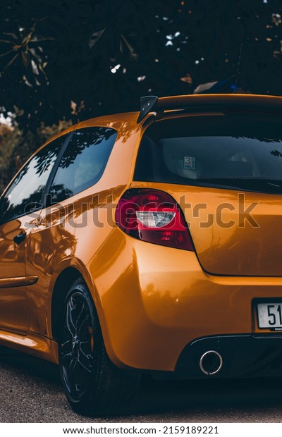 A\
vertical shot of an orange car parked near a\
road