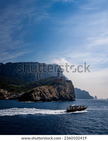 A vertical shot of people on a motorboat sailing near a lighthouse in Capri island, Italy